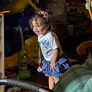 Jenna joined the competition — help win amazing prizes! child, toddler, smiling, curly_hair, pink_bows, white_shirt, blue_skirt, toy, indoor, wooden_floor, happy, playful, person, furniture, household_items, colorful, young_child, cute, joyful, standing