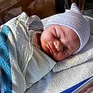 Kyla is registered to the contest to win money with this photo: newborn, baby, sleeping, infant, face, portrait, striped_hat, blanket, swaddled, hospital, bassinette, indoors, soft_lighting, peaceful, resting, closed_eyes, cozy, textile, headwear, photography