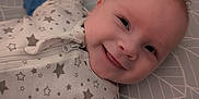 Leon is registered to the contest to win money with this photo: baby, smile, face, infant, onesie, stars, blue_sleeves, cushion, pattern, lying_down, cheeky, tongue_out, cute, happy, child, indoor, soft_light, closeup, skin, head