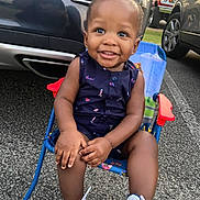 Jayce is registered to the contest to win money with this photo: toddler, child, smiling, sitting, chair, outdoor, asphalt, shoes, sneakers, clothing, person, face, happy, vehicle, car, road, daylight, casual, blue, playful