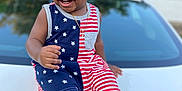 Jayce is registered to the contest to win money with this photo: child, toddler, smiling, sitting, car, hood, outdoor, clothing, romper, stars, stripes, footwear, black_sandals, necklace, happy, person, portrait, daylight, blurred_background, home