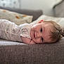 baby, child, clothing, couch, cozy, cute, face, happy, head, home, indoor, infant, lying_down, pillow, portrait, resting, skin, smile, soft_lighting, young