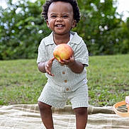 Matteo is registered to the contest to win money with this photo: toddler, child, apple, smiling, outdoor, grass, blanket, barefoot, greenery, happy, cute, clothing, shorts, shirt, nature, daylight, portrait, playful, person, baby