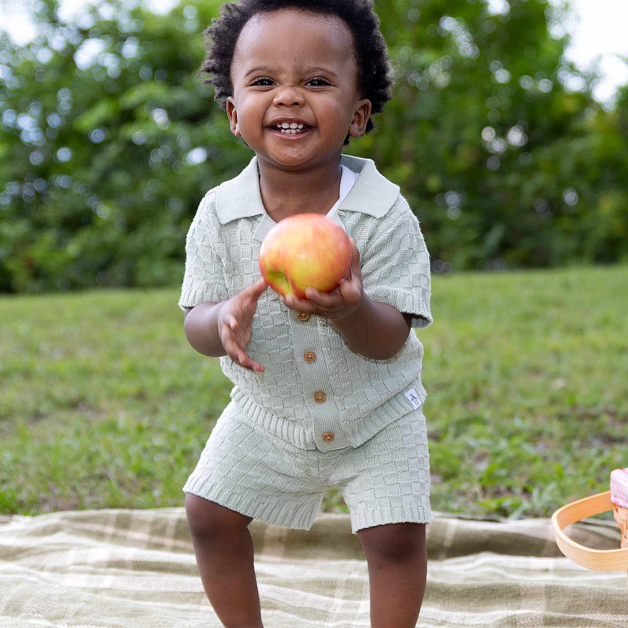 Matteo is registered to the contest to win money with this photo: toddler, child, apple, smiling, outdoor, grass, blanket, barefoot, greenery, happy, cute, clothing, shorts, shirt, nature, daylight, portrait, playful, person, baby