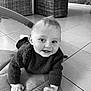 Emilien participe au concours pour gagner de l'argent avec cette photo : baby, child, crawling, smiling, face, hands, wool_sweater, indoor, floor_tiles, mat, wicker_furniture, black_and_white, portrait, cute, toddler, happy, curious, human, young, cozy