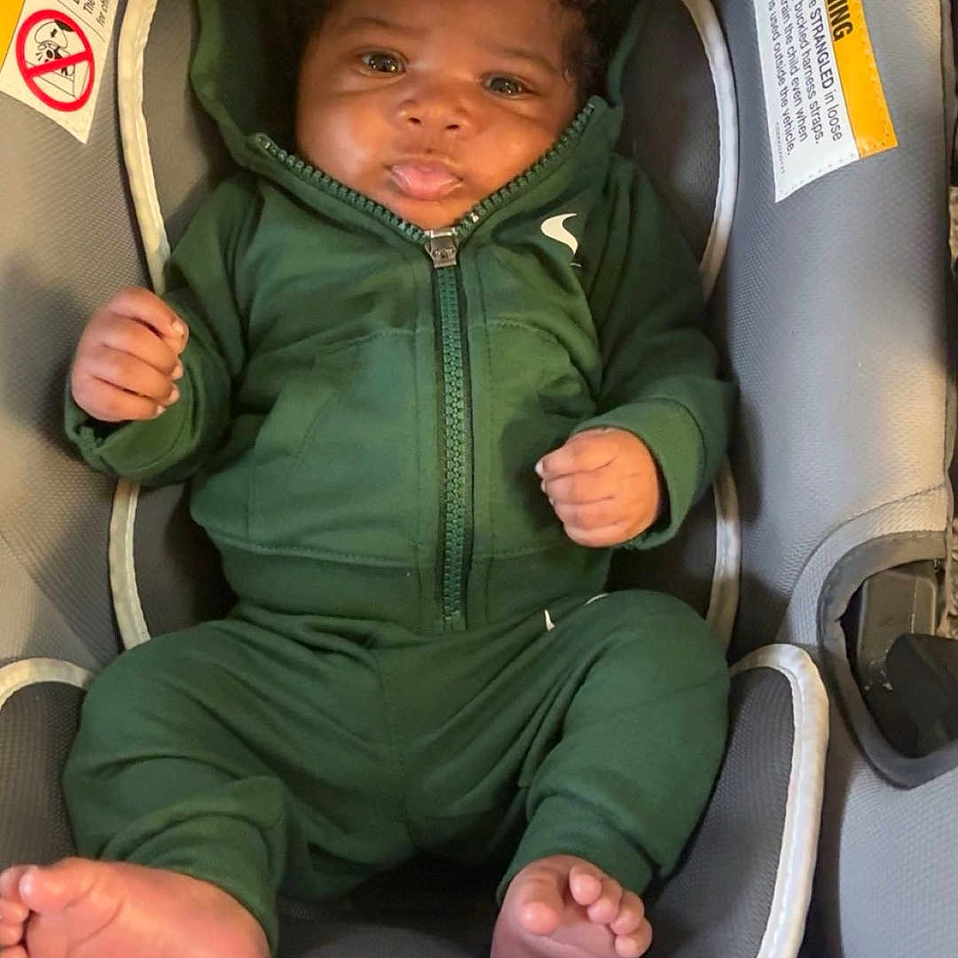 Nas joined the competition — help win amazing prizes! baby, infant, green_hoodie, car_seat, tongue_out, cute, child, smiling, clothing, seat_belt, indoor, infant_clothing, foot, hand, head, face, person, warning_label, fabric, soft