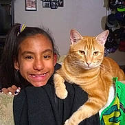 Cheddar is registered to the contest to win money with this photo: girl, child, smiling, cat, orange_tabby, pet, indoor, couch, furniture, portrait, happy, family_photos, wall, hat_collection, home, cozy, casual, black_clothing, long_hair, nail_polish