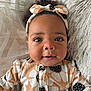 Kamaya is registered to the contest to win money with this photo: baby, infant, face, headband, curly_hair, smile, eyes, clothing, pattern, cushion, blanket, portrait, closeup, cute, child, indoors, soft_texture, happy, person, lying_down