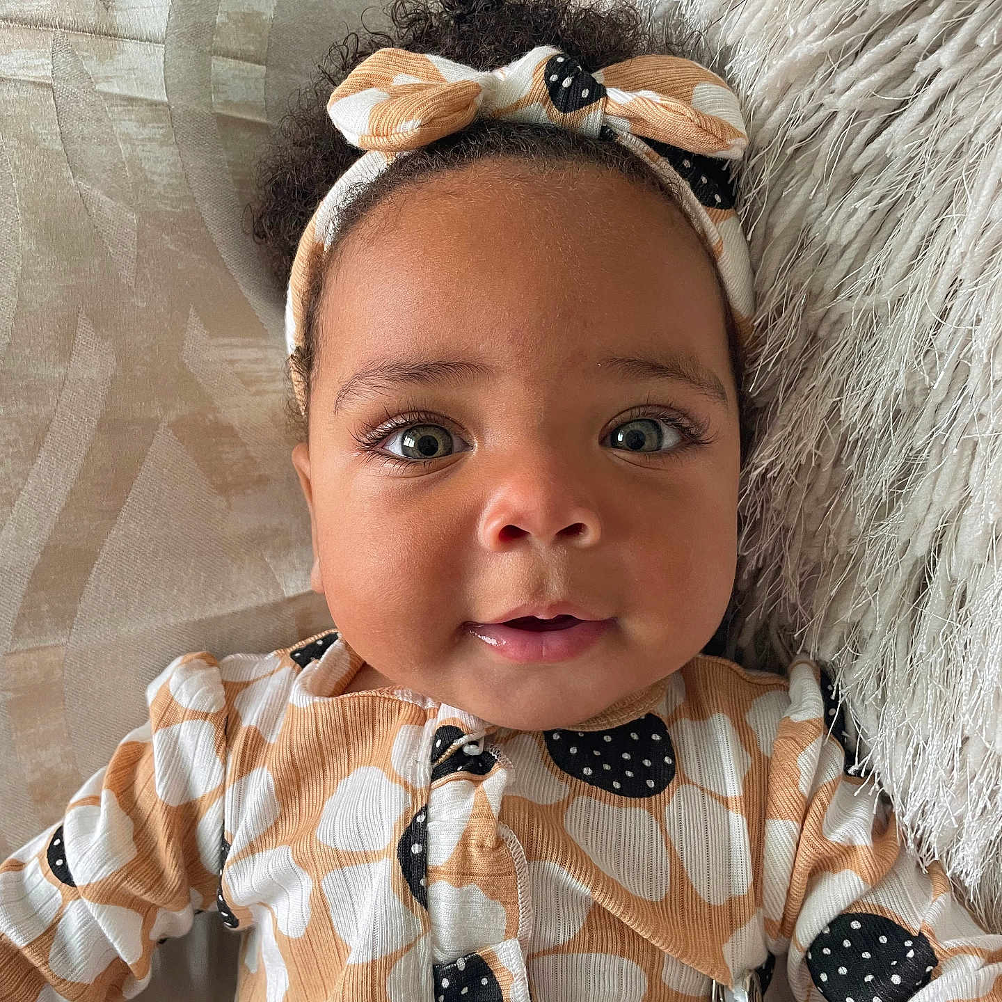 Kamaya is registered to the contest to win money with this photo: baby, blanket, child, closeup, clothing, curly_hair, cushion, cute, eyes, face, happy, headband, indoors, infant, lying_down, pattern, person, portrait, smile, soft_texture