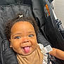 baby, child, stroller, curly_hair, tongue_out, smiling, bib, white_lace, brown_clothing, black_stroller, cute, playful, infant, seatbelt, happy, portrait, indoors, closeup, person, young_child