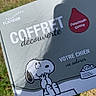 dog, snoopy, cartoon, brochure, packaging, dog_food, pet_product, printed_text, outdoor, grass, lawn, sunlight, shadow, paper, magazine, illustration, advertisement, french_text, red_badge, blue_design