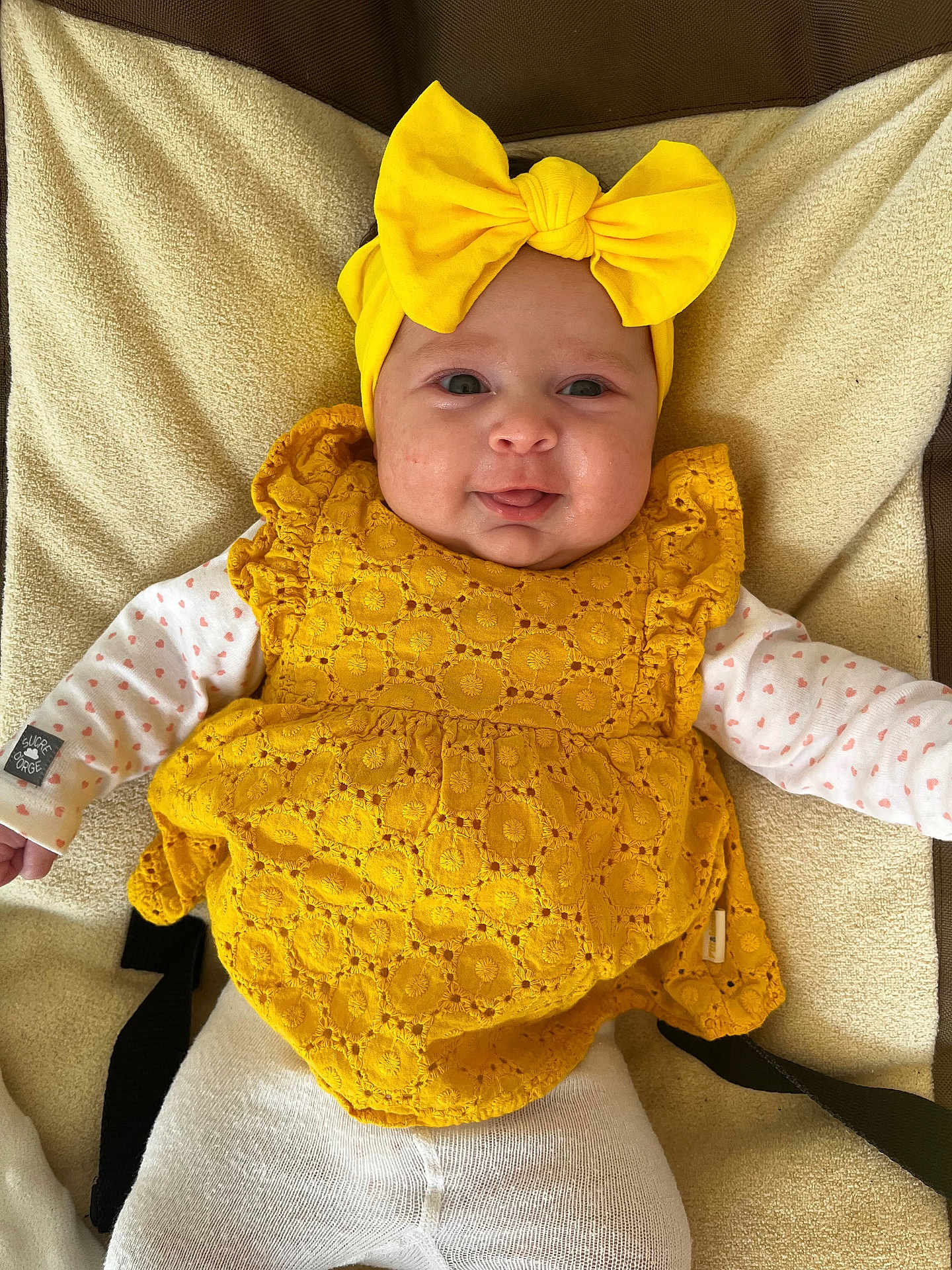 Jade a rejoint le concours — aidez-le/la à gagner de superbes lots ! baby, infant, headband, yellow_bow, yellow_dress, smile, face, eyes, cheeks, blanket, onesie, heart_pattern, sleeves, lying_down, buckle_strap, textile_texture, portrait, indoors, cute, happy