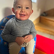 Lyam a rejoint le concours — aidez-le/la à gagner de superbes lots ! child, toddler, smiling, portrait, indoor, face, eyes, hands, sweater, gray_clothing, child_chair, bokeh, background_blur, staircase, happy, cute, shoes, sitting, snack, young_child