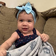 Alona is registered to the contest to win money with this photo: baby, blanket, blue_bow, child, clothing, couch, cozy, cute, face, fun, furniture, happy, headband, holding, indoor, infant, person, portrait, smiling, young_child