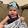 baby, blanket, blue_bow, child, clothing, couch, cozy, cute, face, fun, furniture, happy, headband, holding, indoor, infant, person, portrait, smiling, young_child
