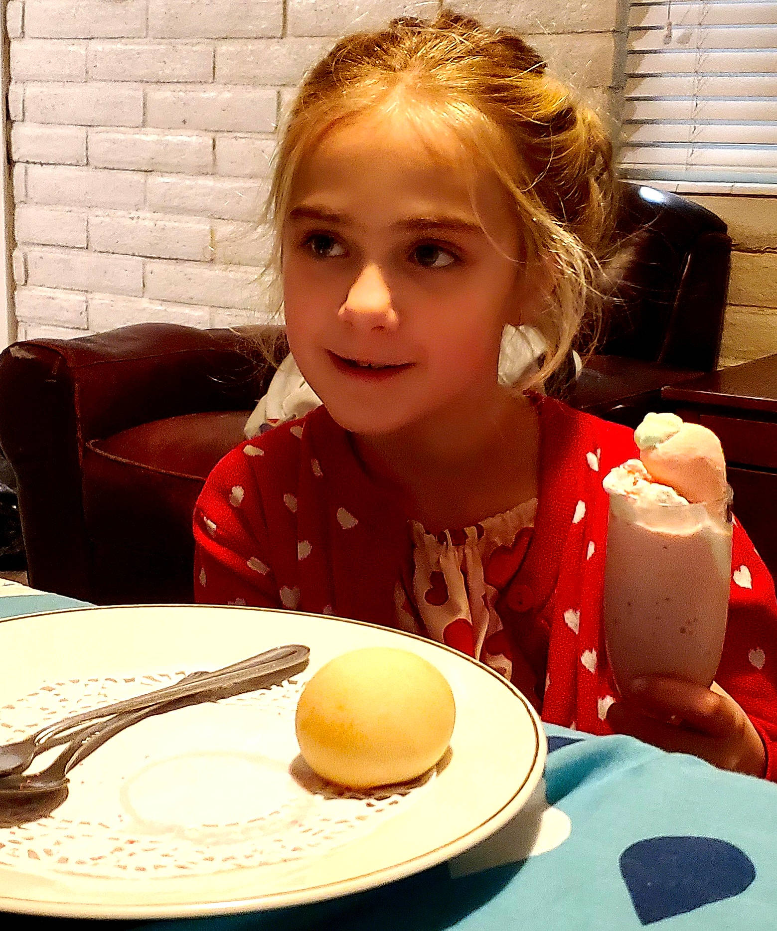 Lola is registered to the contest to win money with this photo: baking, coffee, coffee_cup, cuisine, cup, dishware, drinkware, event, food, hat, person, plate, saucer, serveware, sun_hat, sweetness, table, tableware, toddler, window