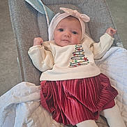 Théa a rejoint le concours — aidez-le/la à gagner de superbes lots ! baby, infant, child, headband, bow, sweater, christmas_tree, red_skirt, white_tights, baby_seat, blanket, cushion, indoor, floor, portrait, cute, smile, clothing, person, relaxing