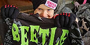 Atreyu is registered to the contest to win money with this photo: child, beanie, gloves, beetlejuice, shirt, toy, indoor, clothing, colorful, smile, young_child, person, hat, pattern, playful, room, floor, winter_wear, red, black