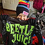child, beanie, gloves, beetlejuice, shirt, toy, indoor, clothing, colorful, smile, young_child, person, hat, pattern, playful, room, floor, winter_wear, red, black