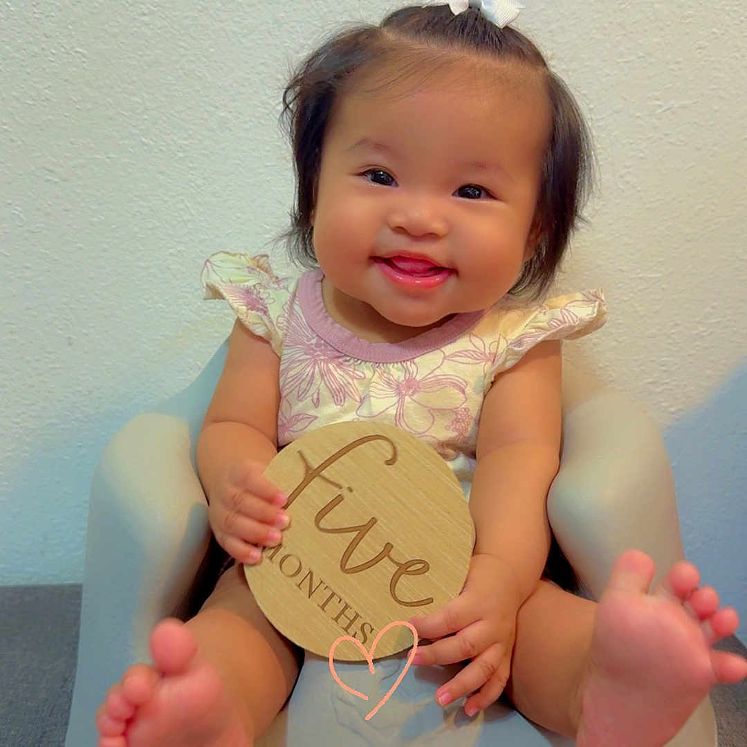 Nevaeh Jade is registered to the contest to win money with this photo: baby, baby_seat, child, clothing, cute, expression, feet, five_months, hair_bow, hands, happy, indoor, infant, person, portrait, sitting, smiling, wall, wooden_sign, young_child