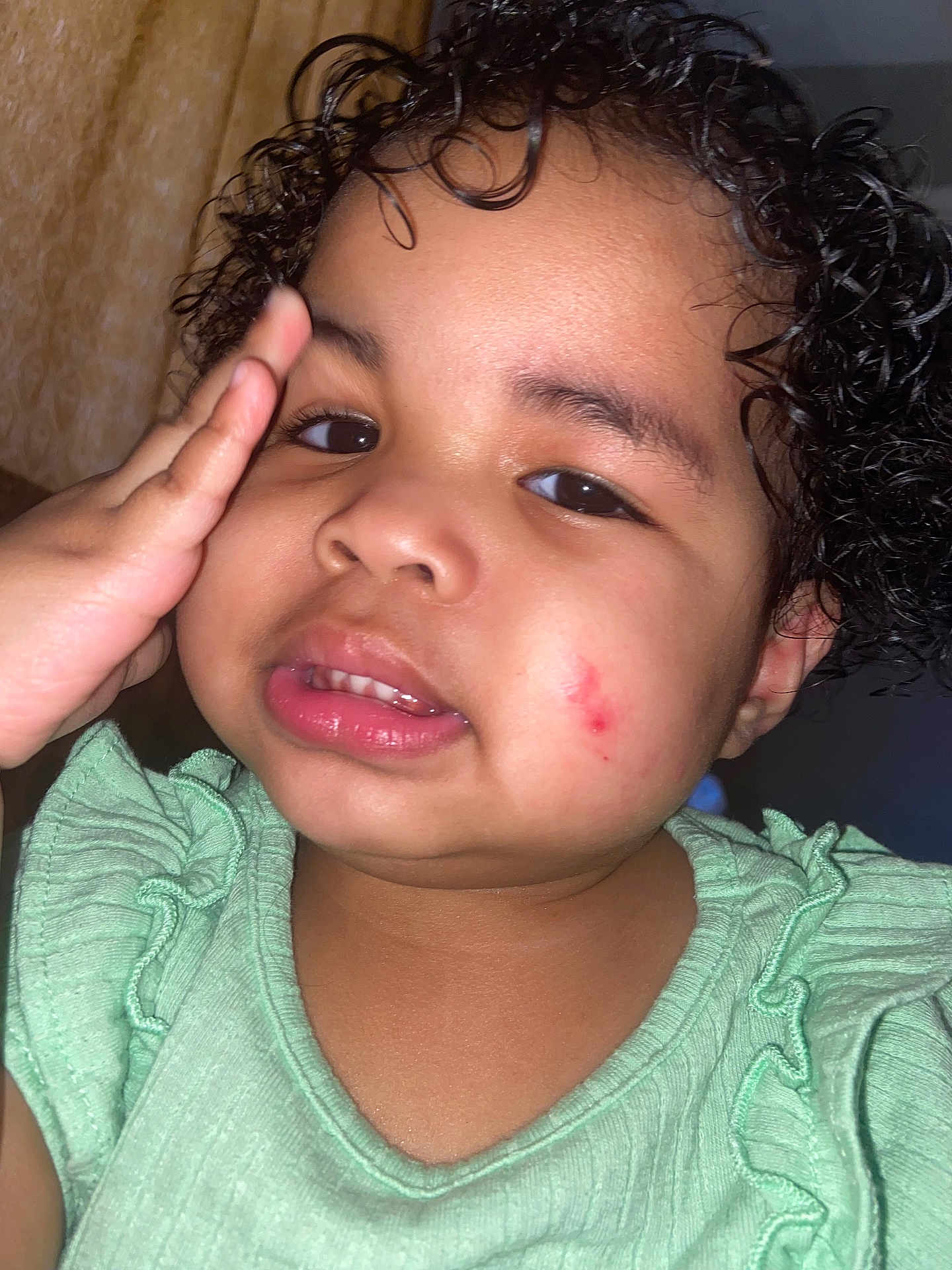 Triana is registered to the contest to win money with this photo: toddler, child, face, curly_hair, green_clothing, hand, indoor, portrait, baby_skin, expression, cute, red_mark, closeup, person, young_child, ruffled_clothing, flash, cheek, smile, human