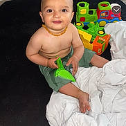 Damon participe au concours pour gagner de l'argent avec cette photo : baby, child, toy, green_toy, colorful_toys, blanket, carpet, floor, indoor, smiling, happy, sitting, shorts, bracelet, necklace, cute, playtime, infant, person, portrait