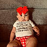 Briley is registered to the contest to win money with this photo: baby, child, red_bow, shirt, text, couch, indoor, infant, clothing, portrait, sitting, cute, expression, home, cozy, red_shorts, person, face, young, casual