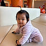 child, toddler, baby, sitting, squatting, portrait, face, smiling, curious, indoor, restaurant, bench, couch, lavender_clothing, fleece, ponytail, keys, remote_control, orange_decor, honeycomb_pattern