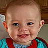 baby, blue_bib, cheerful, child, closeup, cute, expression, eyes, face, happy, head, indoors, infant, person, portrait, red_trim, skin, smiling, wood_background, young_child
