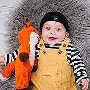 Theo joined the competition — help win amazing prizes! baby, child, smiling, toy, knitted_toy, fox_toy, beanie, hat, yellow_overalls, striped_shirt, black_and_white, happy, lying_down, fluffy_rug, gray_rug, cute, infant, portrait, indoors, cuddling