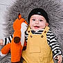 baby, child, smiling, toy, knitted_toy, fox_toy, beanie, hat, yellow_overalls, striped_shirt, black_and_white, happy, lying_down, fluffy_rug, gray_rug, cute, infant, portrait, indoors, cuddling