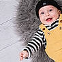 Theo is registered to the contest to win money with this photo: baby, smiling, beanie, striped_shirt, yellow_overalls, furry_rug, happy, blue_eyes, infant, child, cute, portrait, indoor, clothing, button, hand, face, headwear, person, baby_fashion
