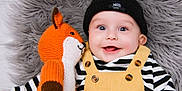 Theo joined the competition — help win amazing prizes! baby, child, smiling, knitted_toy, fox, beanie, yellow_overalls, striped_shirt, happy, cute, soft_blanket, portrait, indoor, close_up, playful, infant, toy, cozy, button, expression
