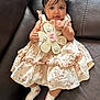 baby, bracelet, child, couch, cute, dress, floral_pattern, flower_shape, hair_clip, hand, holding, indoors, infant, leather, portrait, sign, sitting, smiling, socks, young_child