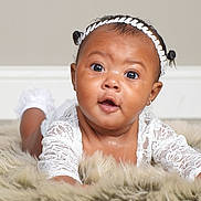 Zamiyah is registered to the contest to win money with this photo: baby, infant, child, face, headband, white_lace, fur_rug, skin, eyes, mouth, earrings, lying_down, portrait, curious, cute, adorable, indoors, soft_texture, closeup, expression