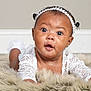 baby, infant, child, face, headband, white_lace, fur_rug, skin, eyes, mouth, earrings, lying_down, portrait, curious, cute, adorable, indoors, soft_texture, closeup, expression