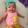 baby, infant, headband, bow, pink_tank_top, yellow_shorts, chick_design, smiling, lying_down, blanket, purple_blanket, white_bedspread, cute, happy, child, person, indoors, soft_lighting, closeup, casual_clothing
