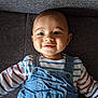 baby, child, smiling, denim_overalls, striped_shirt, couch, indoor, portrait, happy, infant, face, person, clothing, seated, cute, young, one_child, head, skin, eyes