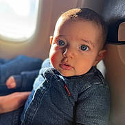 Amir participe au concours pour gagner de l'argent avec cette photo : baby, child, denim, jacket, airplane, window, seat, face, blue_eyes, curious, light, portrait, infant, clothing, cute, indoor, person, sitting, closeup, young