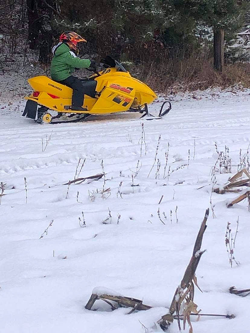 Wesley is registered to the contest to win money with this photo: automotive_tire, freezing, fun, geological_phenomenon, grass, nature, outdoor_power_equipment, person, piste, plant, recreation, sled, slope, snow, snowmobile, sports, tree, twig, winter, winter_sport