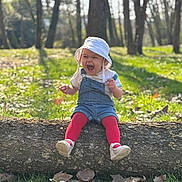 Svetlana participe au concours pour gagner de l'argent avec cette photo : baby, bokeh, bucket_hat, child, daisies, denim_overalls, forest, grass, joyful_expression, laughing, log, nature, outdoor, portrait, red_tights, sitting, sunlight, toddler, trees, white_shoes