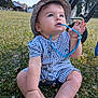 baby, child, grass, outdoor, sunhat, romper, blue_eyes, sunglasses, chewing, stroller, nature, daylight, summer, field, legs, hands, face, curious, sitting, clothing