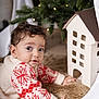 baby, child, christmas_lights, christmas_tree, crawling, curly_hair, cute, decor, festive, fur_rug, holiday, holiday_season, indoor, miniature_house, portrait, red_pattern, soft_lighting, sweater, warm, white_sweater
