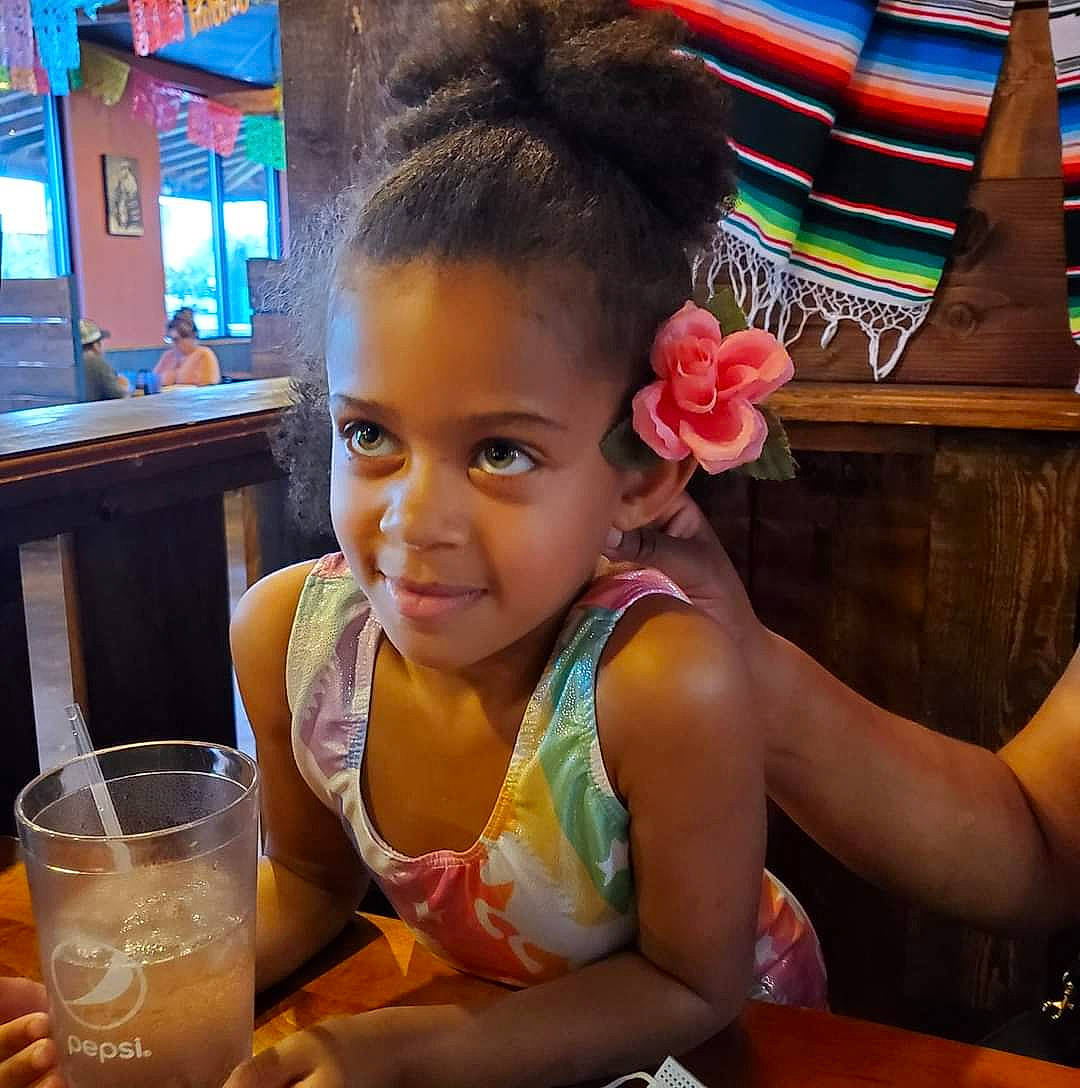 Jianna is registered to the contest to win money with this photo: afro, braid, breakfast, chair, child, distilled_beverage, drink, drinking, drinkware, fun, hair_accessory, happy, joy, leisure, non_alcoholic_beverage, person, sitting, smile, table, tableware