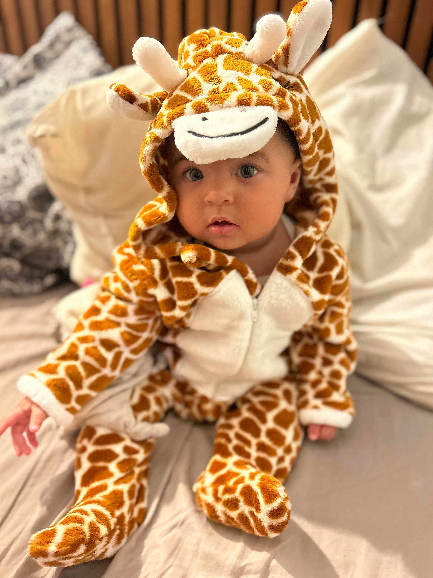 Norah a rejoint le concours — aidez-le/la à gagner de superbes lots ! baby, child, giraffe_costume, onesie, bed, pillow, blanket, indoor, cute, infant, soft_toy_style, animal_print, childrens_clothing, portrait, sitting, looking_at_camera, cozy, warm, plush, adorable