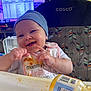 baby, high_chair, bib, food, messy, smiling, hat, indoor, feeding, hands, face, child, person, jar, table, expression, cute, clothing, furniture, happy