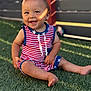toddler, child, smiling, grass, outdoor, sunlight, happy, face, baby, red_clothing, blue_clothing, striped_clothing, stars, barefoot, sitting, fence, summer, daylight, portrait, cute
