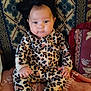 Wisdom is registered to the contest to win money with this photo: baby, infant, child, leopard_print, onesie, headband, black_bow, couch, pillow, blanket, patterned, sitting, cute, face, portrait, indoors, soft_lighting, clothing, person, young_child