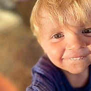 Leythen participe au concours pour gagner de l'argent avec cette photo : child, toddler, smiling, blonde_hair, face, eyes, close_up, portrait, natural_light, curious, happy, casual_clothing, messy_face, skin, person, young_child, cute, indoors, warm_tone, soft_focus