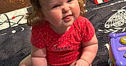 Chloe is registered to the contest to win money with this photo: baby, blanket, bows, carpet, child, chubby_cheeks, cute, expression, girl, home, indoor, infant, person, playtime, polka_dot, red_onesie, remote_control, sitting, smiling, toy